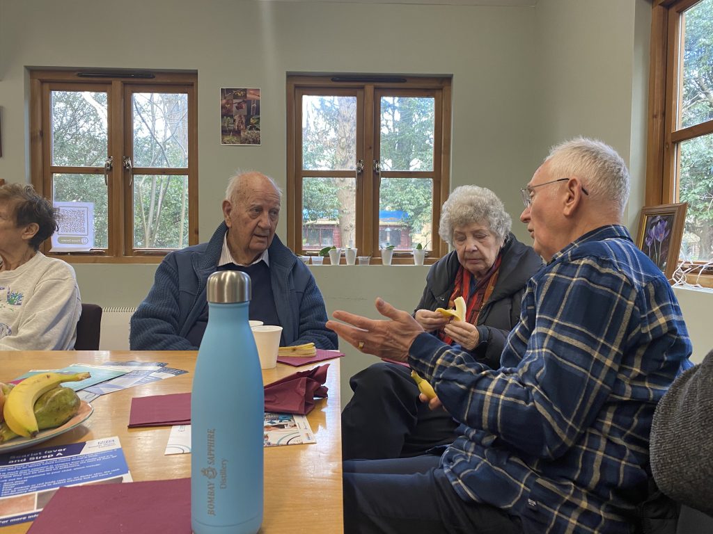 Elderly people gathered around a table drinking tea and talking to each other 