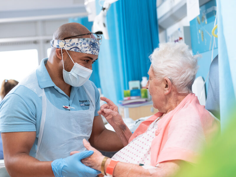 A nurse talking to a patient in her bed at Kingston Hospital