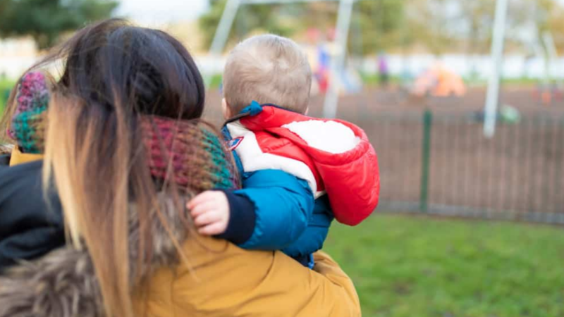 Mother holding young child. They are outside.
