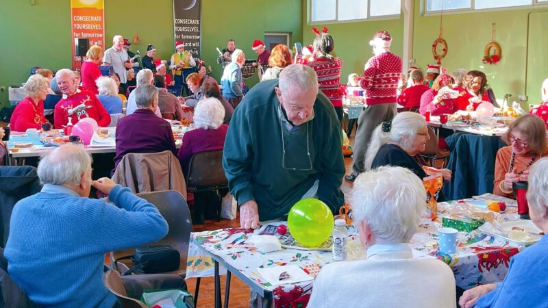 Church hall filled with people sitting at tables talking and eating