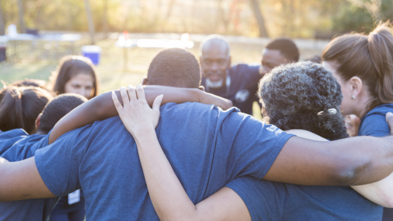 Group of volunteer standing in a circle with their arms around each other's shoulders.